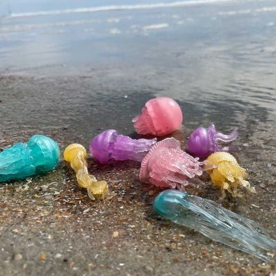 Natuurlijkleuk Toob glow-in-the-dark jellyfish toys in assorted translucent colors on a beach.
